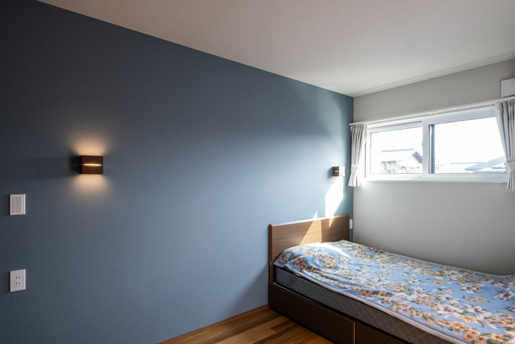 落ち着いたブルーのアクセント壁が印象的な寝室。柔らかな光が入る心地よい空間。