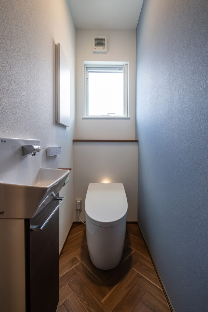 ブルーの壁紙とヘリンボーン床が特徴のトイレ空間。小窓から自然光が入る明るいトイレ。
