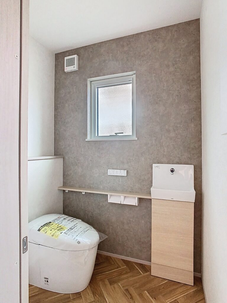 石目調のクロスが空間を引き締める、ホテルライクなトイレ。木目調の手洗いカウンターや全館空調により、快適で清潔感のある空間に。｜富士K邸